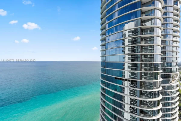 Curved glass high-rise condo tower along a turquoise sea and blue sky.