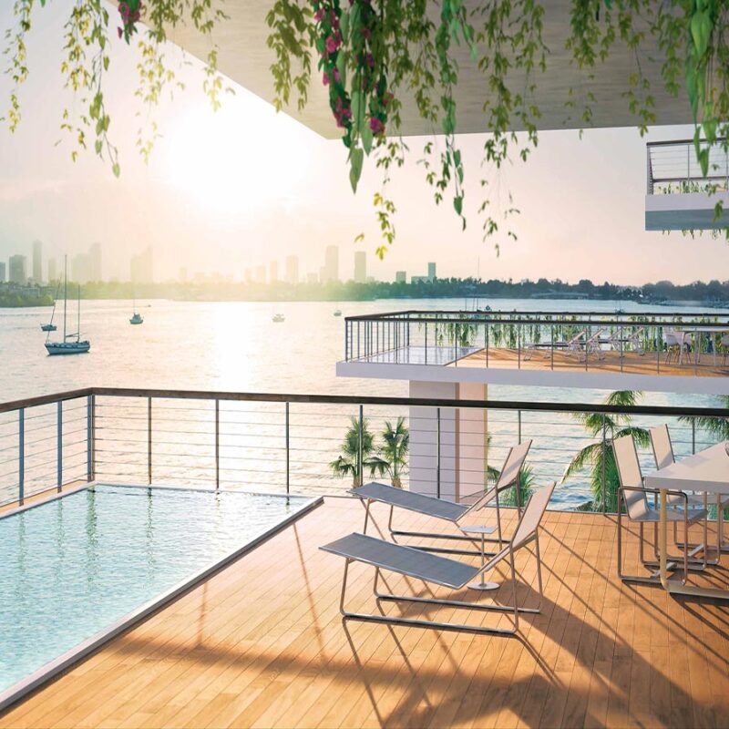 Modern waterfront terrace with a rectangular pool, sun loungers, and a dining table, overlooking boats and a city skyline at sunset.