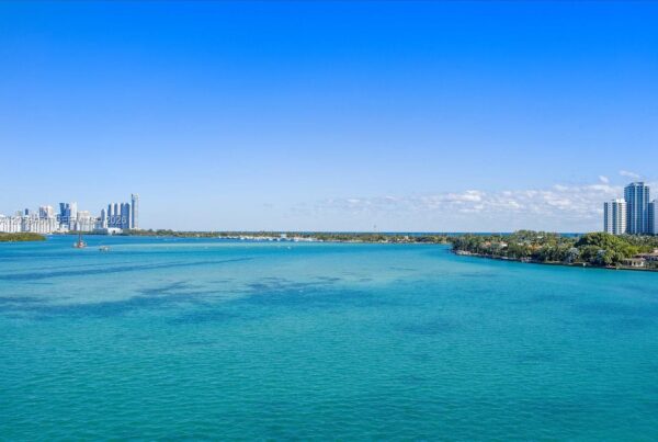Coastal city skyline along turquoise sea under a clear blue sky on a sunny day.
